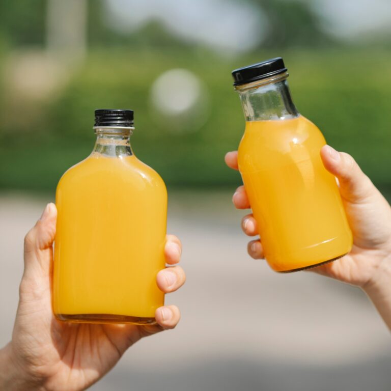 two hands holding bottle of orange juice